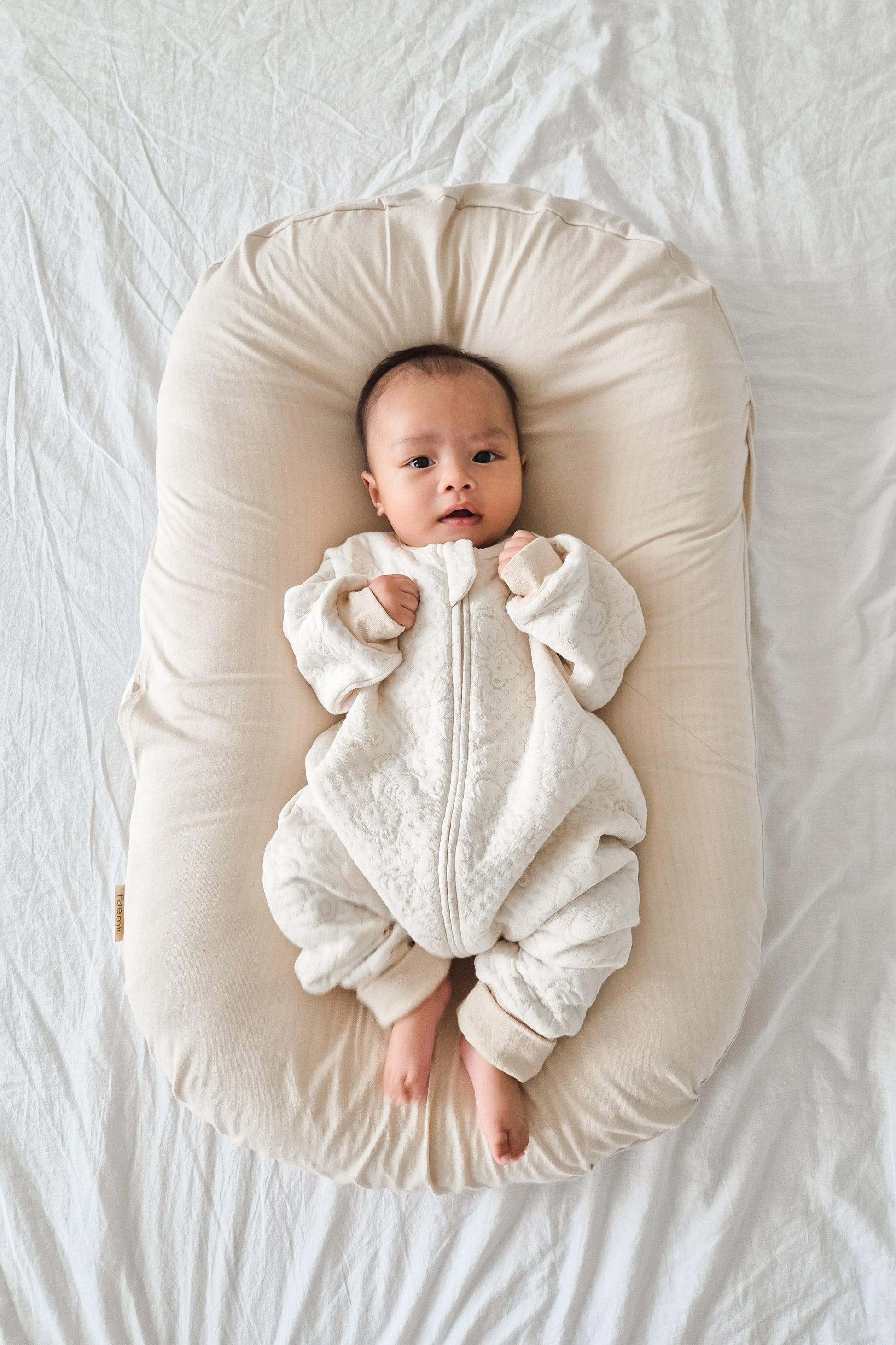 baby in sleepsuit laying on a baby nest