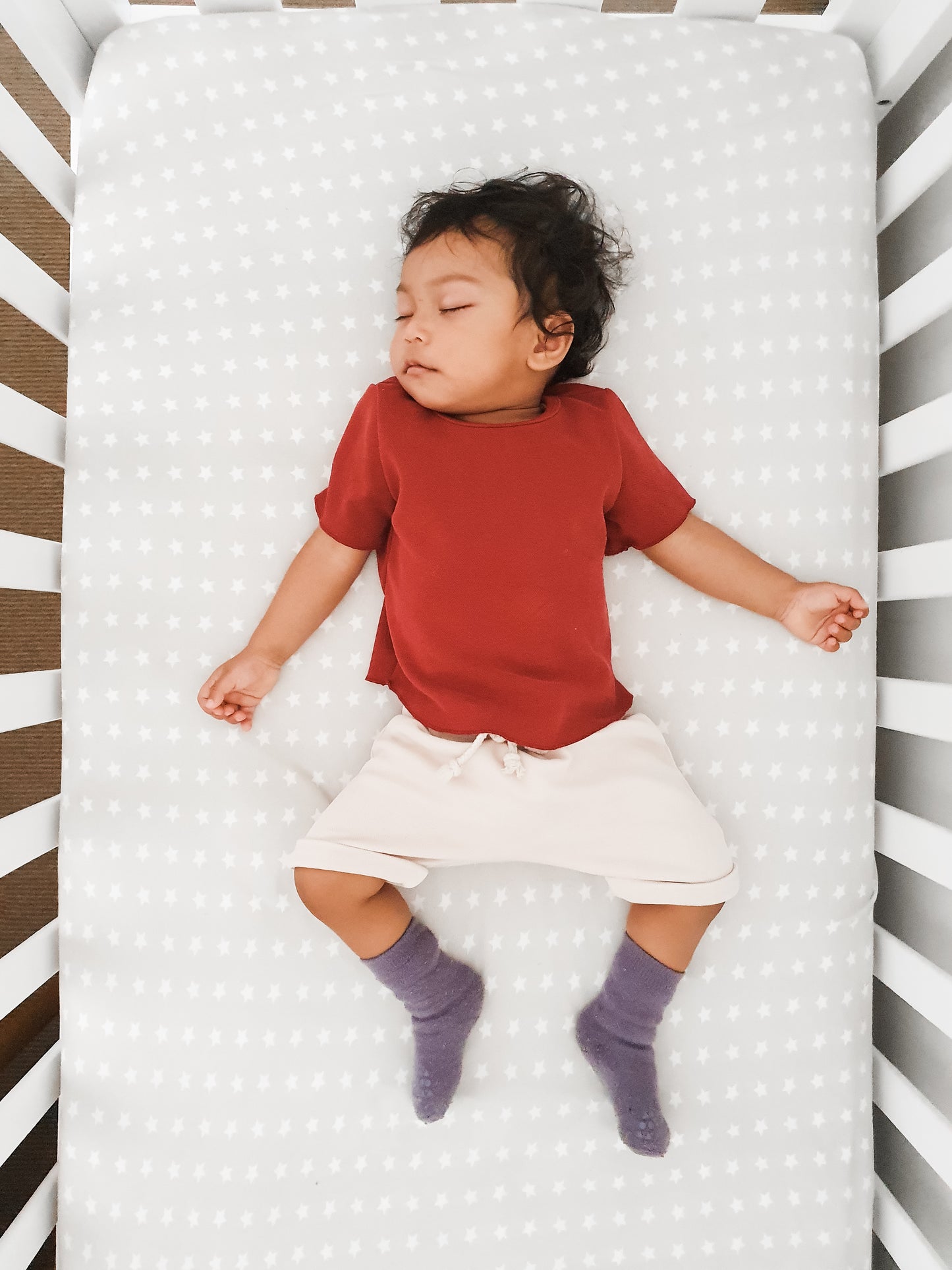 baby boy sleeping in a crib wearing maroon top and beige shorts