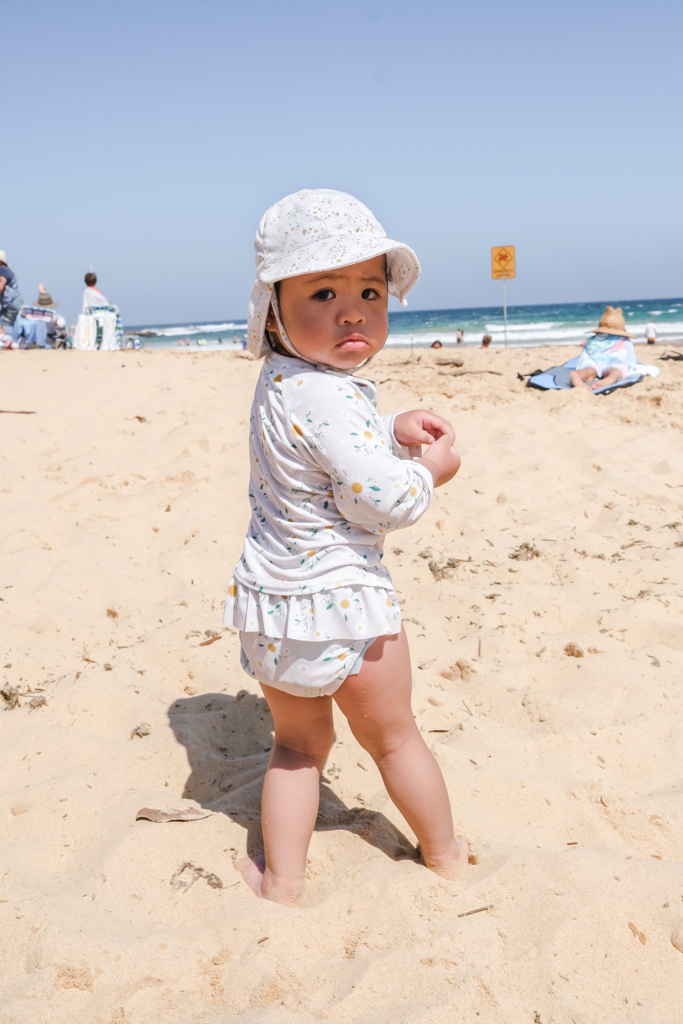 baby girl wearing matching hat and swimsuit at the beach