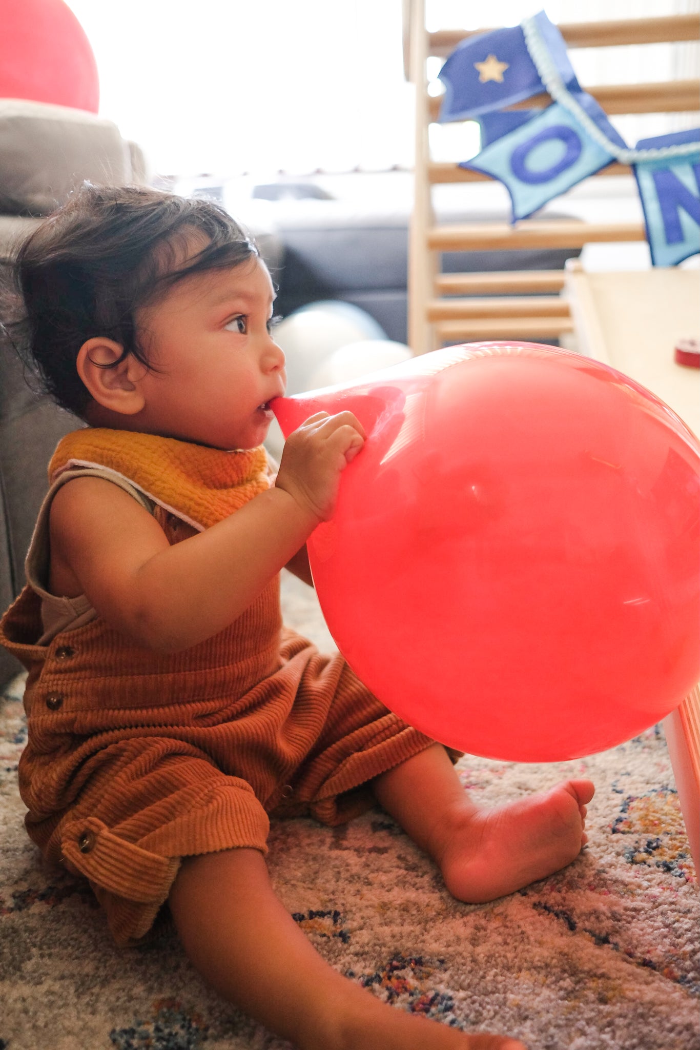 Baby wearing corduroy overalls and biting red balloon