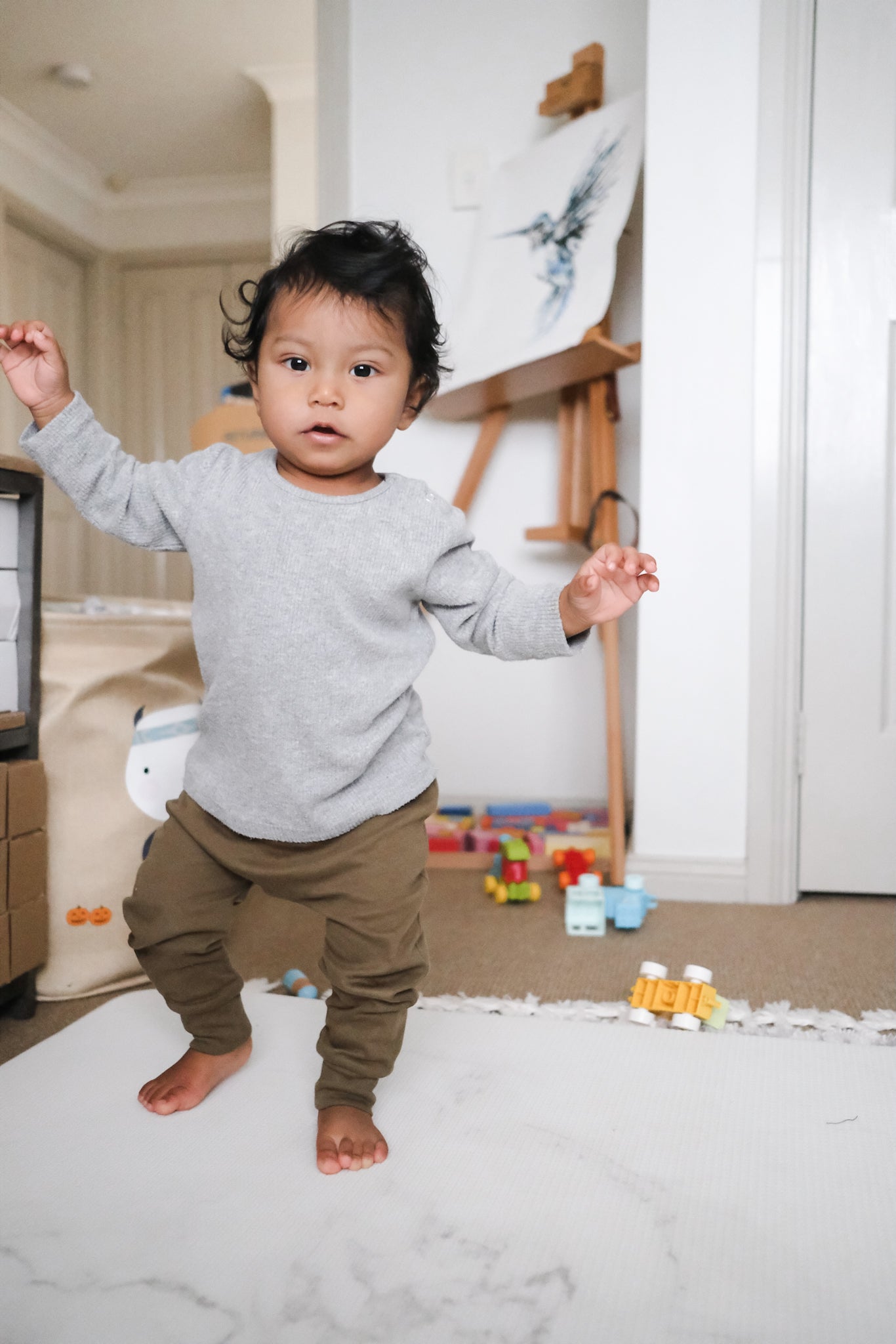 Baby walking wearing khaki leggings and grey sweatshirt