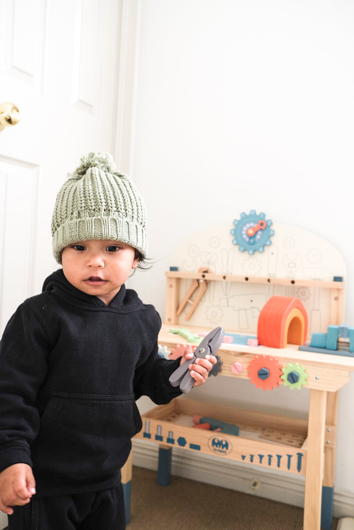 baby wearing knitted beanie playing with wooden toys