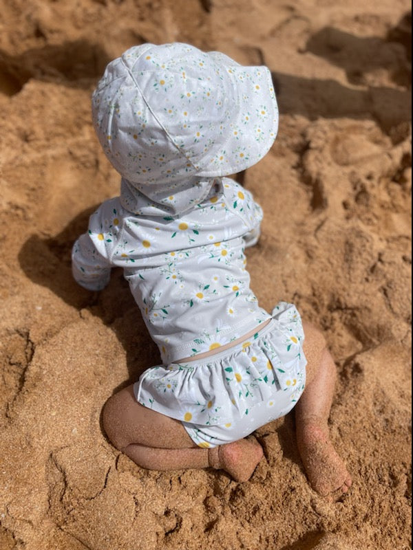 baby girl crawling on the sand wearing matching swimsuit and hat